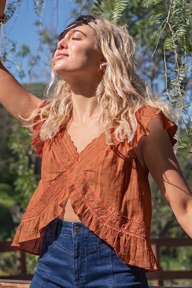Woman in a rust-colored top and blue jeans standing outdoors with trees in the background