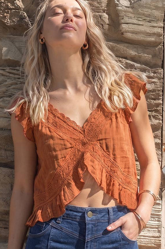 Woman wearing an orange lace top and blue jeans standing against a stone wall.