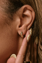 Close-up of an ear wearing gold hoop earrings with a finger touching the earlobe.