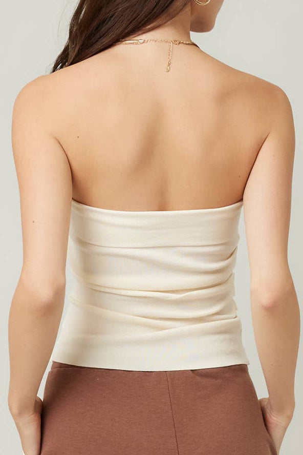Woman wearing a white strapless top and brown pants against a plain background