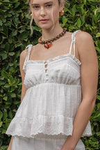 Woman wearing a white lace top standing against a green leafy background