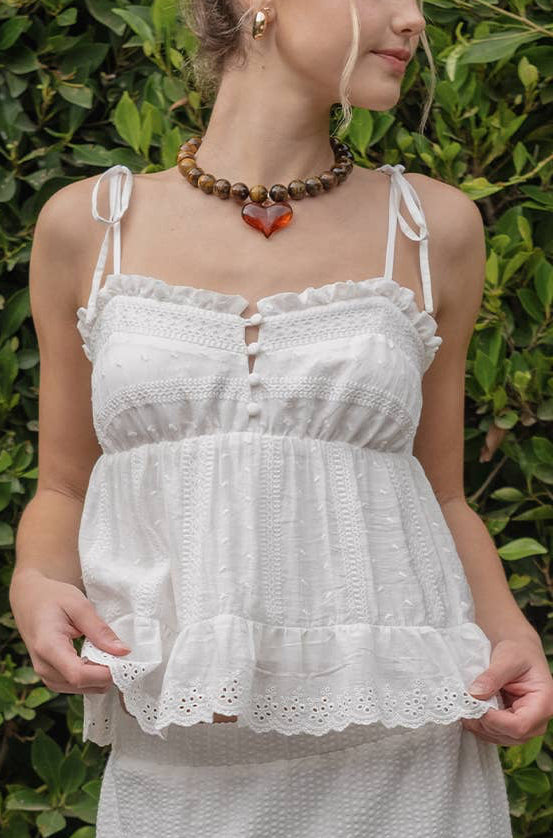 Woman wearing a white lace top and skirt against a green hedge.