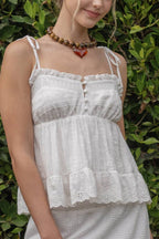 Woman wearing a white lace dress standing against a green leafy background