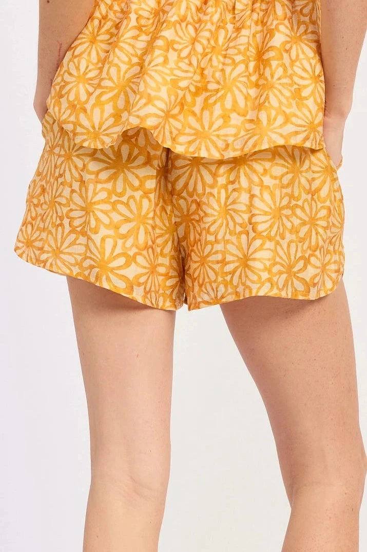 Person wearing yellow floral shorts and white sneakers on a plain background