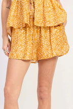Person wearing a yellow floral short with white sneakers and socks on a light purple background