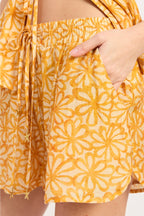 Yellow floral patterned shorts with a hand in the pocket on a white background