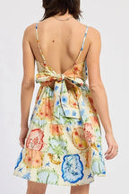 Woman wearing a colorful floral dress with a tie-back detail on a white background