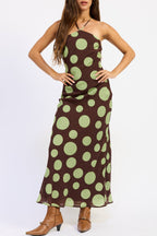 A woman modeling a brown halter-neck maxi dress with a large light green polka dot pattern, paired with brown pointed-toe heeled boots, against a plain white studio background.