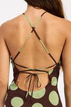 Back view of a woman wearing a brown and light green polka dot top with crisscross back straps and tie details.