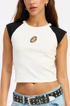 Woman wearing a white and black sleeveless top with a logo, paired with blue jeans.