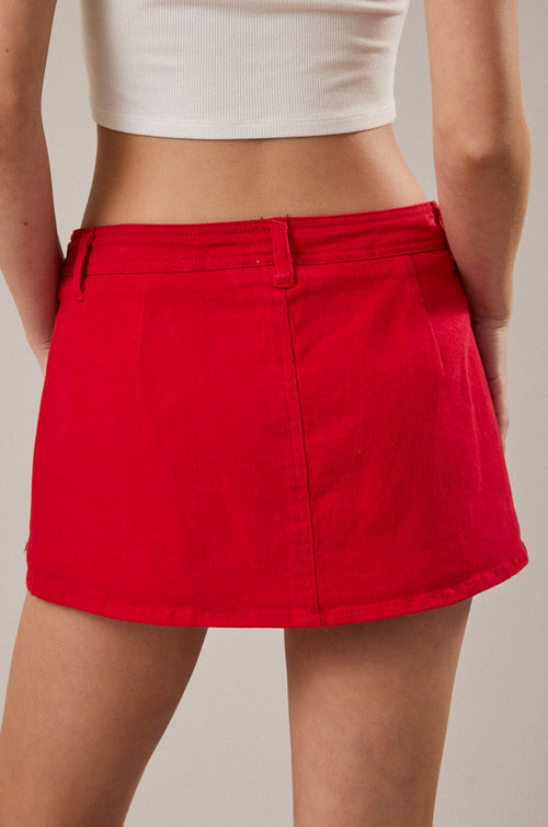 Person wearing a red skirt and white top against a neutral background