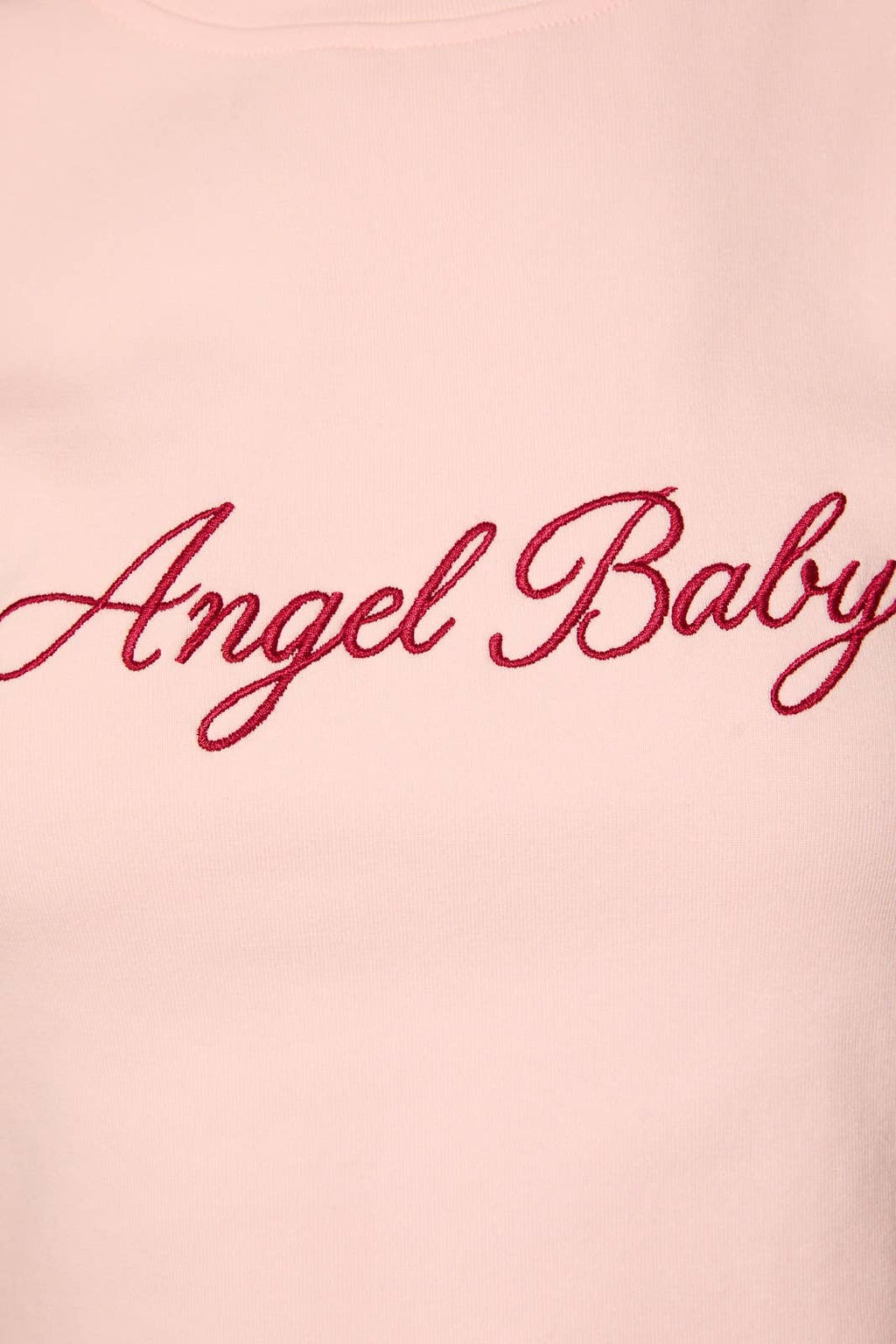 A close-up of a light pink sweatshirt featuring the words 'Angel Baby' embroidered in red cursive script across the chest.