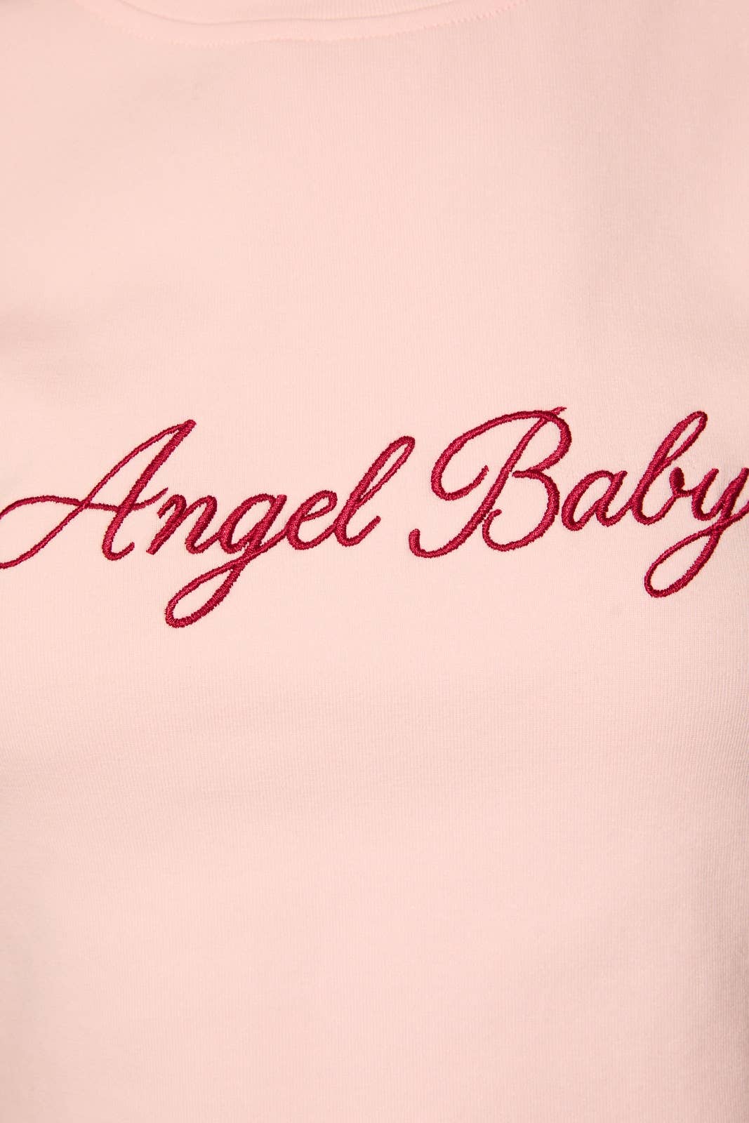 A close-up of a light pink sweatshirt featuring the words 'Angel Baby' embroidered in red cursive script across the chest.