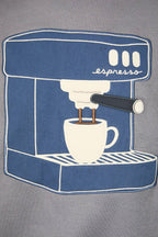 A close-up of a gray fabric garment featuring a large blue and white embroidered patch depicting an espresso machine with a cup and the word 'espresss'.
