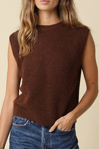 A woman modeling a sleeveless brown knit top and blue denim shorts against a plain beige studio background.