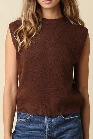A woman modeling a brown sleeveless knit top and blue denim shorts against a solid beige studio background.