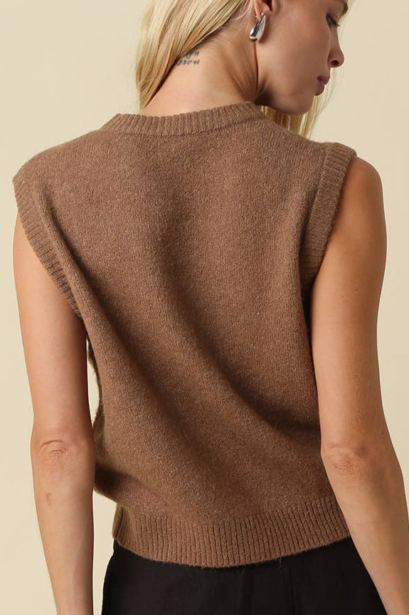 A woman shown from the back wearing a sleeveless brown knit sweater vest over a black top, set against a solid beige background.