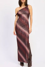 A woman modeling a one-shoulder mesh maxi dress with a dark red and black abstract pattern, paired with dark brown boots, against a plain white studio background.