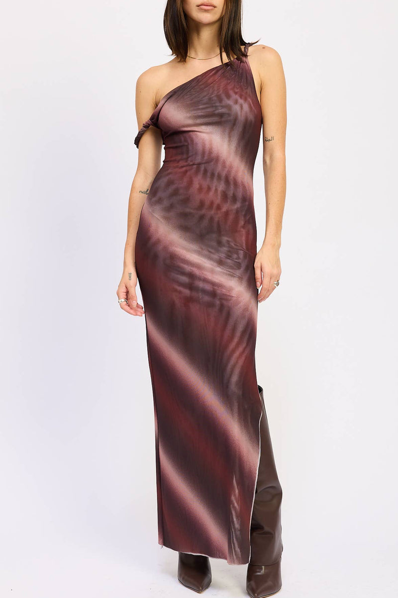 A woman modeling a one-shoulder mesh maxi dress with a dark red and black abstract pattern, paired with dark brown boots, against a plain white studio background.