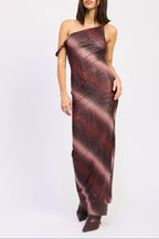 A woman modeling a one-shoulder maxi dress with a dark abstract pattern in deep burgundy, brown, and black, paired with dark brown pointed-toe boots, against a plain white studio background.