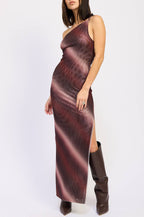 A woman modeling a one-shoulder, floor-length dress with a dark burgundy and brown abstract pattern, paired with dark brown knee-high boots, against a plain white studio background.