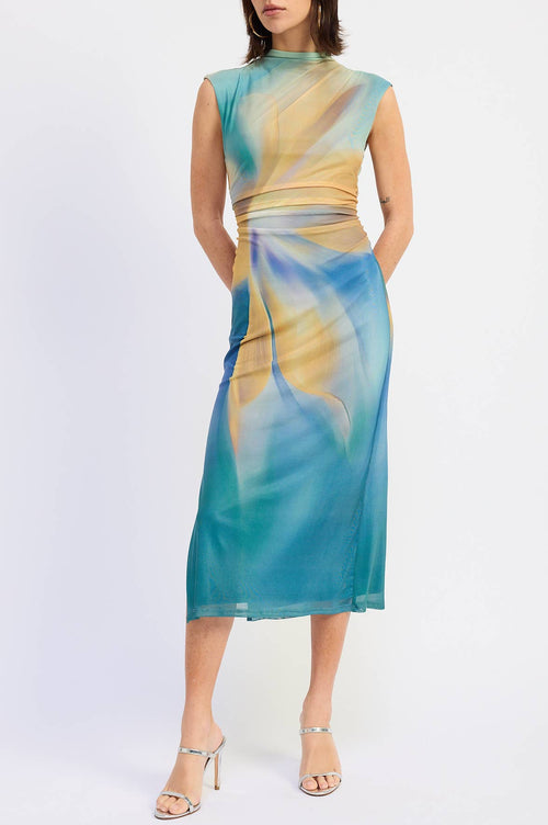 A woman modeling a sleeveless midi dress with a high mock neck and an abstract watercolor-like print in teal, blue, and beige, paired with clear strap high-heeled sandals against a plain white studio background.