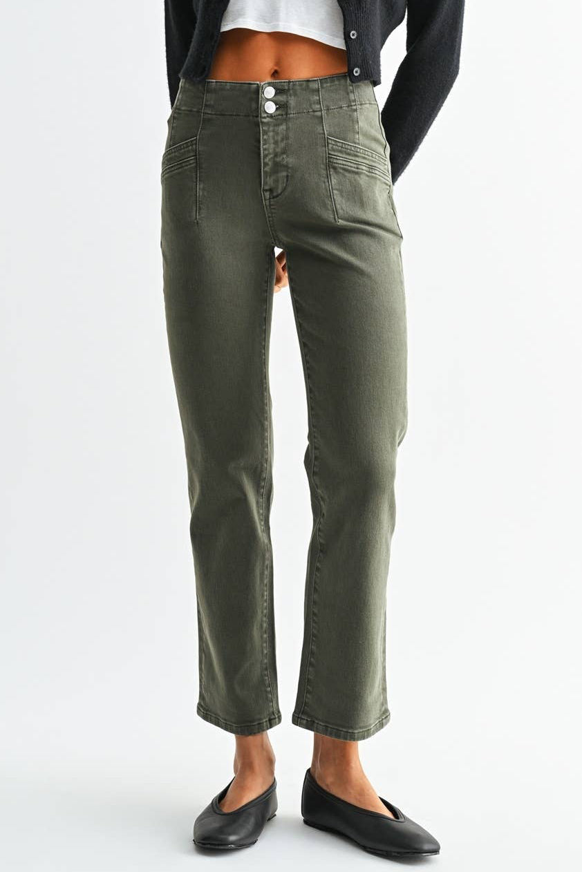 A woman modeling a pair of olive green cropped straight-leg jeans, styled with a black cardigan, white crop top, and black flats, against a light gray studio background.