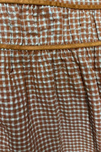 Close-up of a brown and white gingham patterned fabric with a tan elastic waistband.
