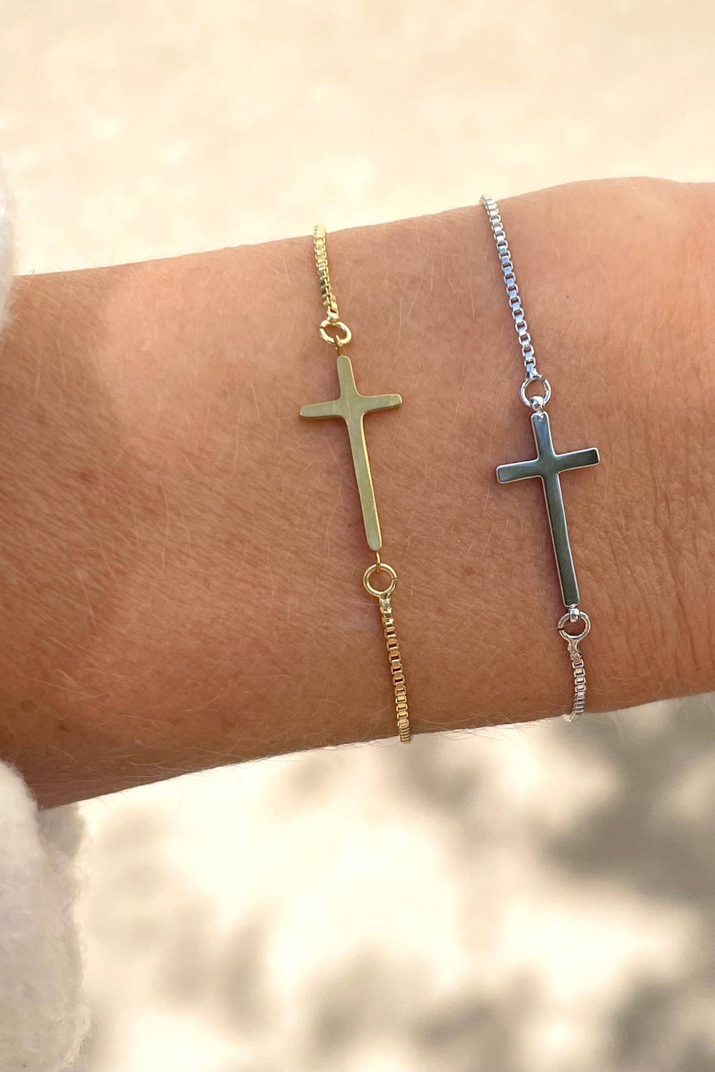 Two cross-shaped bracelets on a wrist against a neutral background