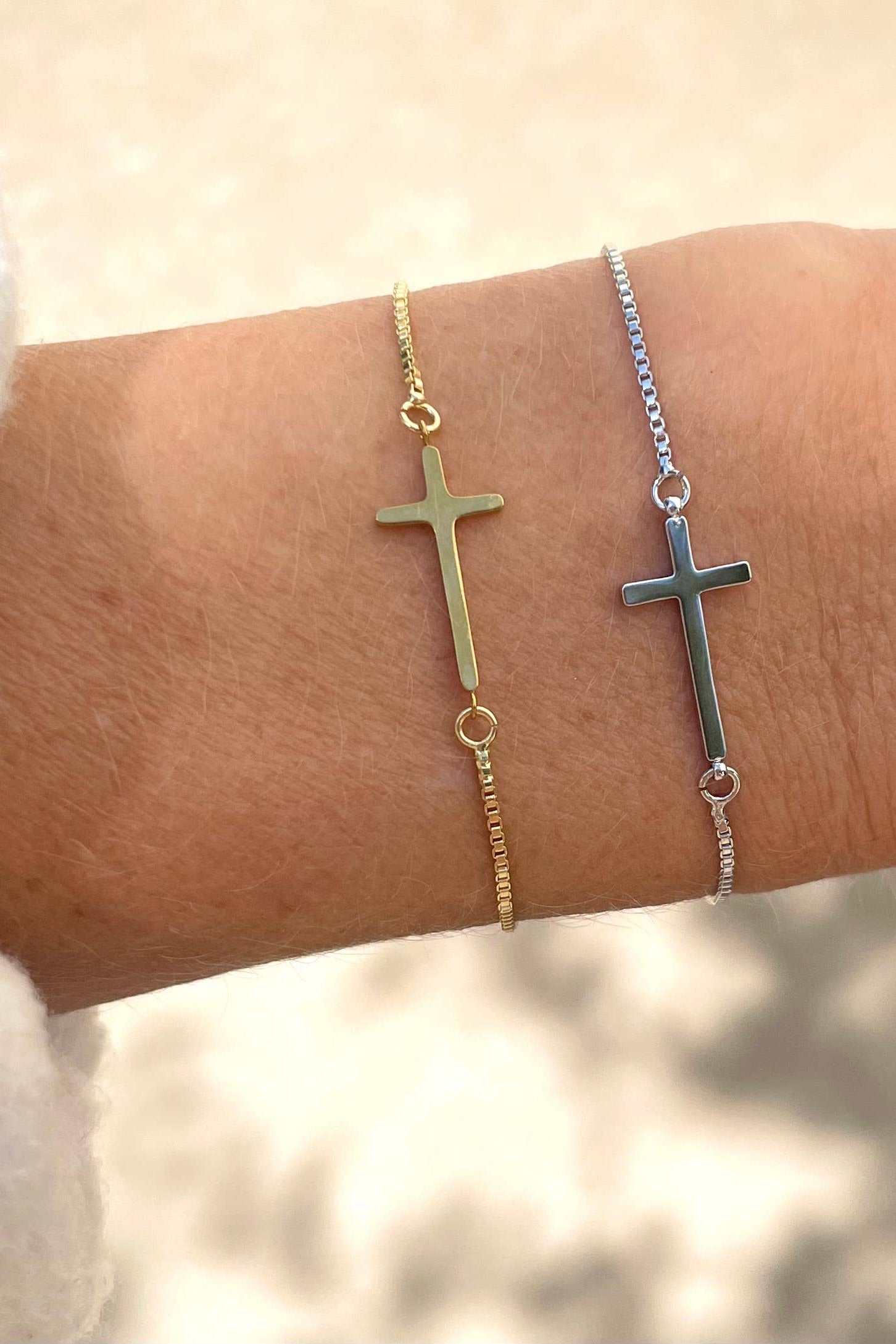 Two cross-shaped bracelets on a wrist against a neutral background