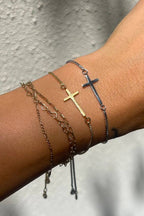 Close-up of a wrist wearing multiple gold and silver bracelets with cross designs on a neutral background.