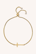 Gold bracelet with a small cross charm on a white background