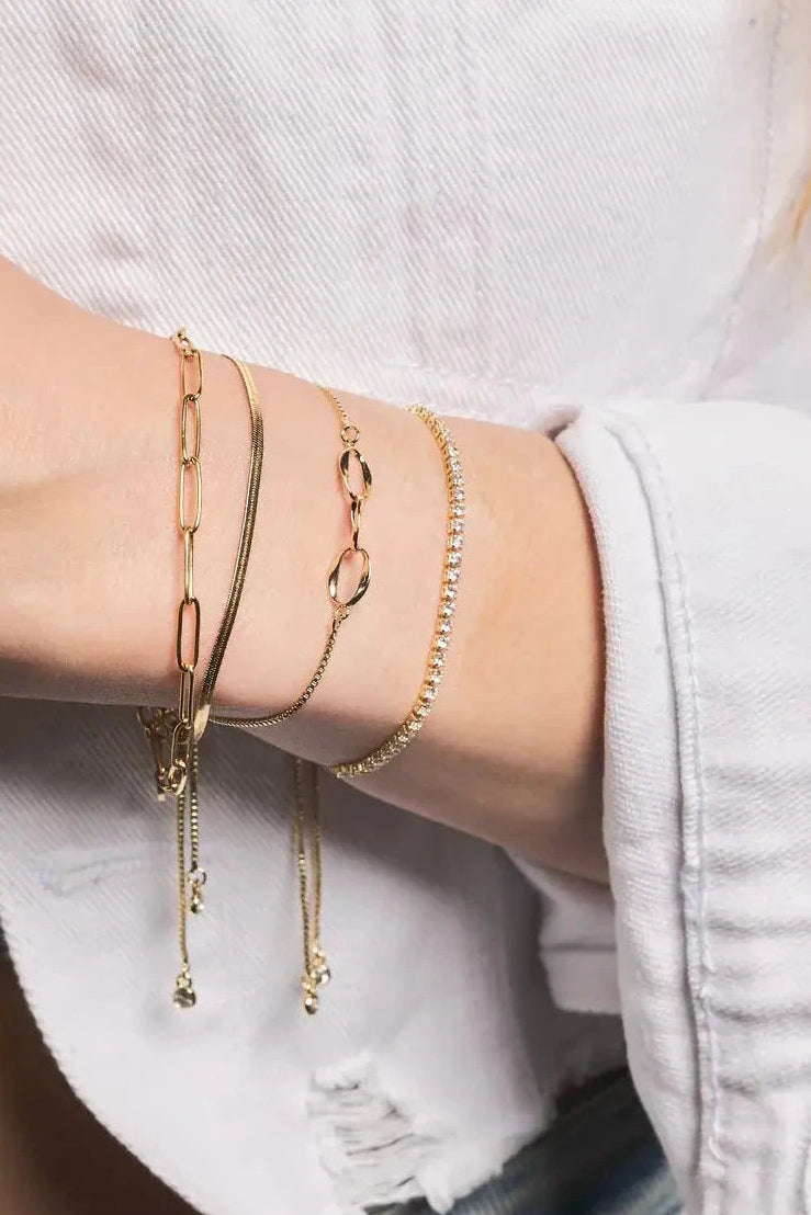 Close-up of a person's wrist wearing multiple gold bracelets on a neutral background