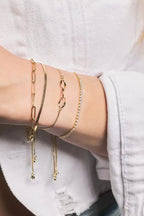 Close-up of a person's wrist wearing multiple gold bracelets on a neutral background