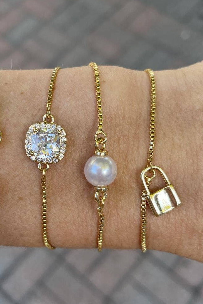 Four gold bracelets with different designs on a wrist against a blurred background