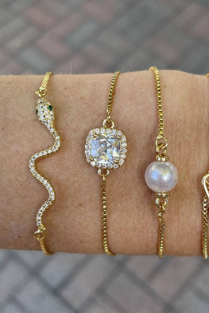 Four gold bracelets with different designs on a wrist against a blurred background