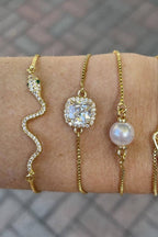 Four gold bracelets with different designs on a wrist against a blurred background