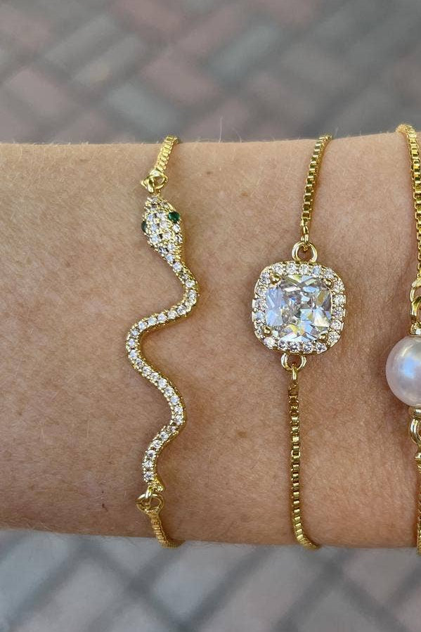 Four gold bracelets with different designs on a wrist against a blurred background