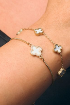 Gold bracelet with clover-shaped charms on a wrist against a dark background