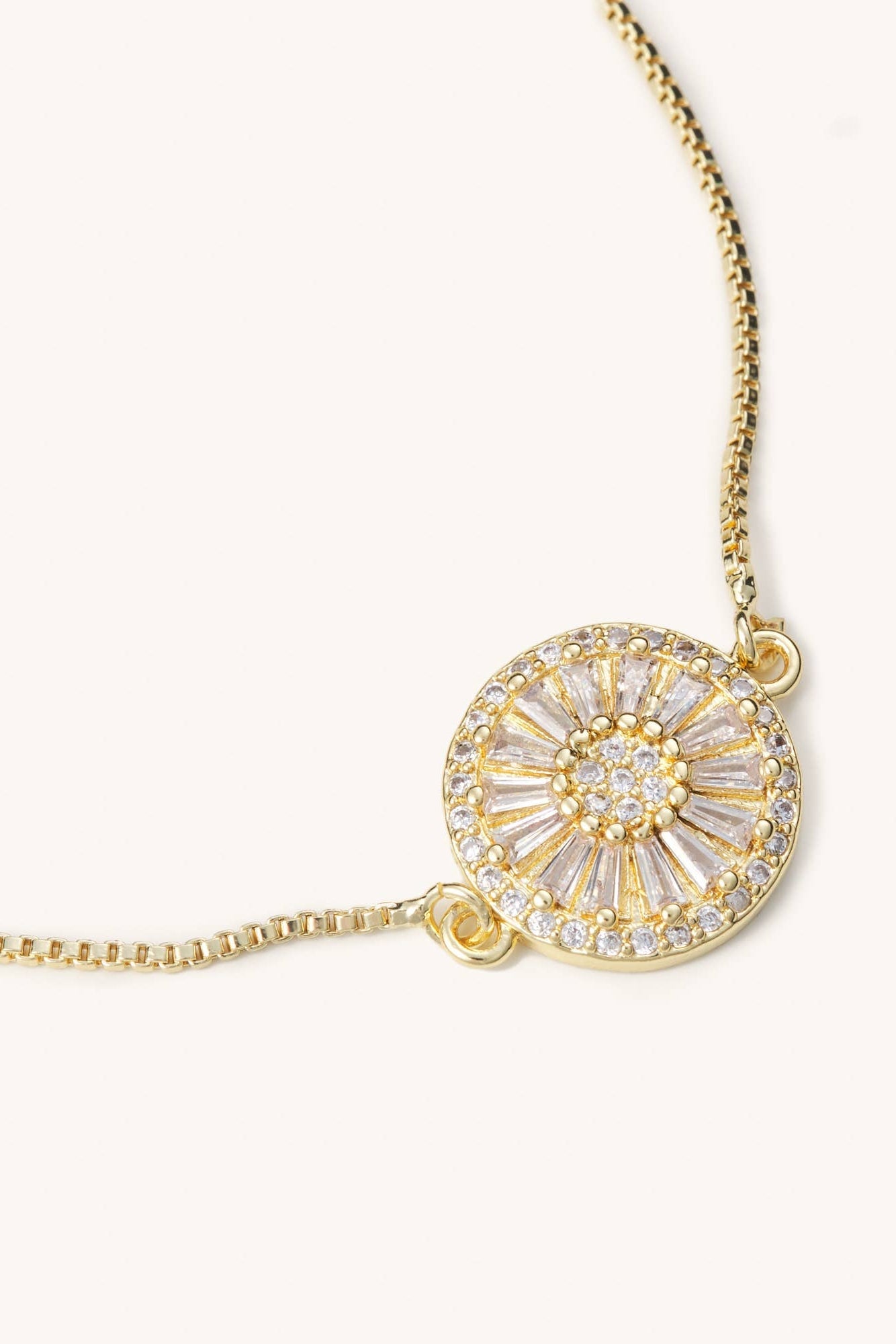 Gold bracelet with a circular pendant on a white background