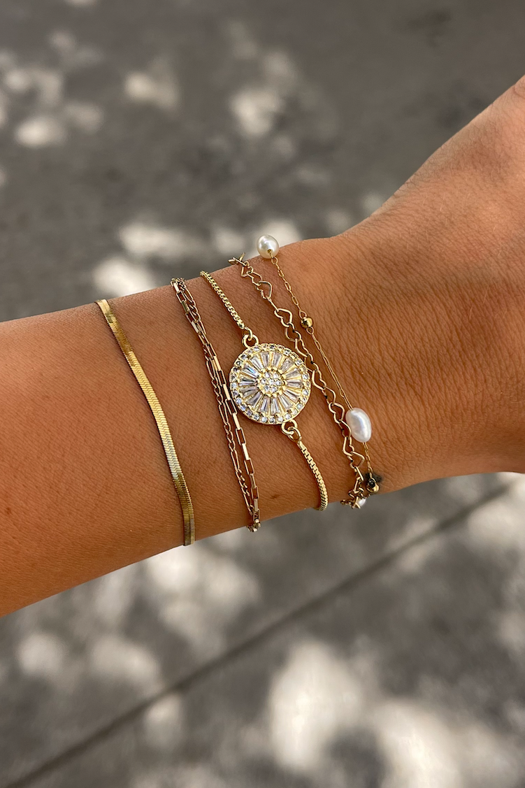 Hand wearing multiple gold bracelets on a blurred outdoor background