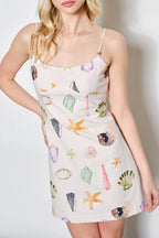 Woman wearing a sleeveless dress with colorful shell pattern against a white background