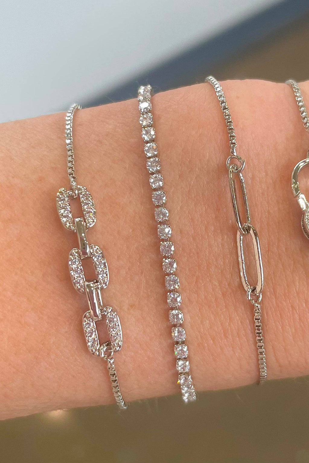 Three silver bracelets on a wrist with a blurred background