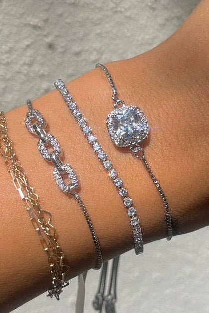 Close-up of a wrist wearing multiple silver bracelets against a neutral background