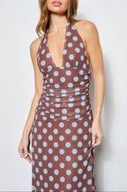 Woman wearing a brown dress with blue polka dots against a plain background