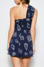 Woman wearing a navy blue dress with white patterns on a plain background