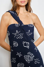 Woman wearing a navy blue one shoulder dress with white ocean sea-themed patterns on a plain background
