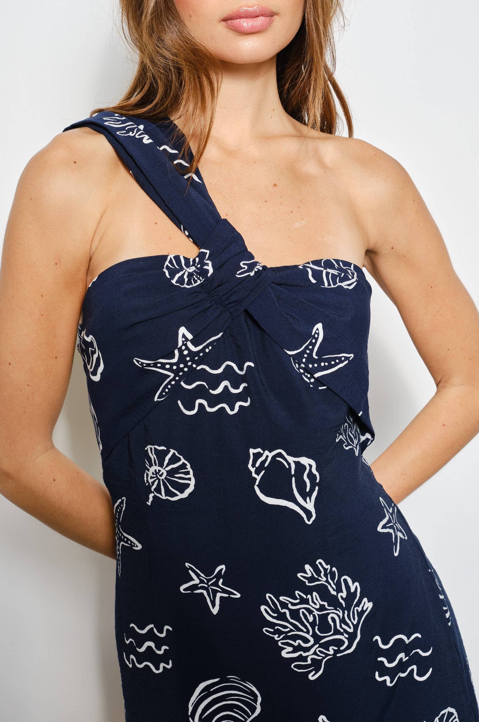 Woman wearing a navy blue one shoulder dress with white ocean sea-themed patterns on a plain background