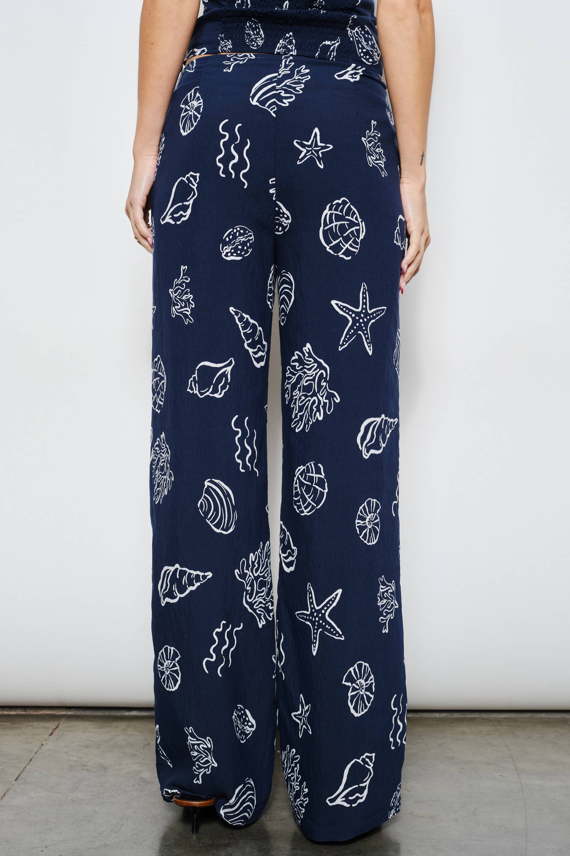 Navy blue pants with white sea-themed pattern worn by a person against a plain background