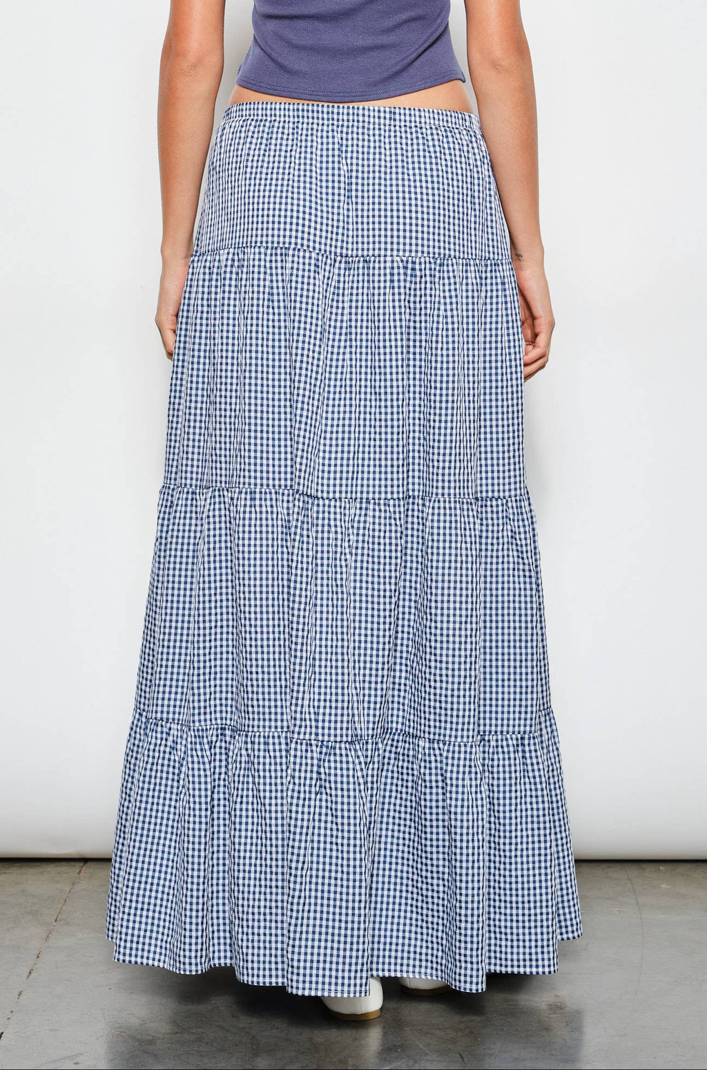 Person wearing a blue tiered skirt and purple top on a white background